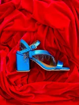 Sandalias de cuero gamuzado color azul, con taco ancho y tiras cruzadas en el empeine decoradas con flecos de cuentas. Cuentan con pulsera regulable al tobillo con hebilla metálica.