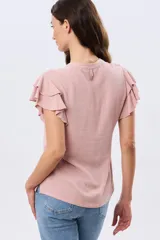 Camisa de lino y viscosa color beige, con cuello mao, escote en V y botones frontales de madera. Presenta mangas cortas con volados delicados.