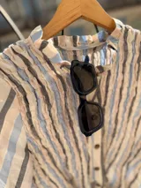Camisa de manga larga con diseño a rayas verticales en tonos azul, gris y crema. Presenta un cuerpo con frunces elásticos decorativos, cuello con volados y puños con elástico y terminación en volado. Incluye cierre frontal con botones.