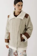 Gamulán de paño en color beige jaspeado con detalles en cuero sintético marrón y forro de corderito sintético blanco. Presenta cierre frontal cruzado, cuello solapa, bolsillos laterales y puños con vuelta.