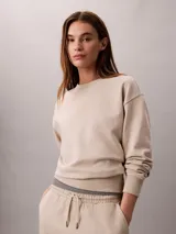 Buzo de felpa Calvin Klein de color beige, con cuello redondo, manga larga y detalles de canalé en cuello, puños y bajo. Presenta un emblema con logo texturizado en el pecho.