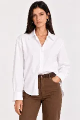 Camisa blanca de algodón, de corte amplio y mangas largas con puños abotonados, cuello clásico y cierre frontal de botones.