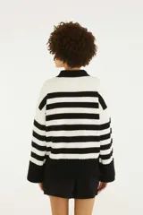 Sweater de punto con diseño a rayas horizontales blancas y negras, cuello alto y puños anchos. Cuenta con un bordado frontal en el centro que representa un loro sobre hojas tropicales y el texto "Farm Rio".