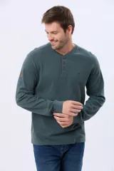 Remera de algodón texturada color gris oscuro, de manga larga, con cuello redondo y botones en la parte frontal. Presenta un pequeño logo bordado en el pecho y un parche decorativo en la manga izquierda.