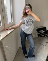 Remera blanca de manga corta, con cuello redondo y diseño gráfico estampado en el pecho que incluye texto y palmeras.