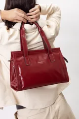 Cartera mini tote de cuero vacuno color bordó, con acabado charol, doble asa de mano y estructura rígida.