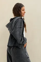 Campera crop estilo hoodie con capucha, cierre frontal completo y efecto acid wash en color negro, de mangas largas amplias y calce holgado.