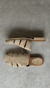 Zuecos de punta cuadrada, confeccionados en gamuza beige con diseño de tiras entrelazadas tipo huarache y suela plana marrón.