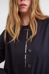 Campera corta oversize de color negro, confeccionada en algodón, con mangas largas, cuello redondo, cierre frontal de botones y bajo con elástico fruncido.