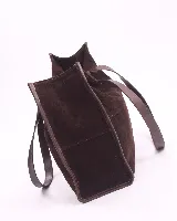 Bolso tipo shopper de gran tamaño, confeccionado en cuero gamuzado color marrón. Presenta estructura rectangular con bordes reforzados en cuero liso oscuro, doble asa de hombro y cierre mediante botón magnético.