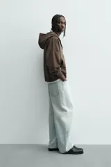 Sudadera con capucha y cierre de cremallera frontal, color marrón oscuro, de corte holgado (boxy fit) y manga larga. Presenta bolsillos frontales de vivo y acabados en rib en puños y bajo.