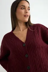 Cardigan de punto con diseño de trenzas, color beige, con escote en V, cierre frontal de botones negros y mangas largas con puños acanalados.