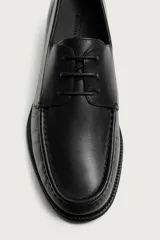 Zapato tipo náutico negro fabricado en piel, con horma redonda, empeine con cordones sutiles y suela a tono con ligero tacón.