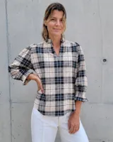 Blusa de algodón con estampado de cuadros en tonos beige, negro y azul. Presenta cuello alto con detalle de volados, escote en V y mangas tres cuartos abullonadas con puños elásticos terminados en volados.