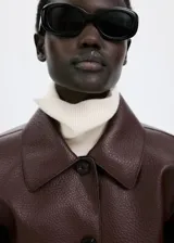 Chaqueta de cuero sintético marrón con cuello camisero, cierre frontal con botones oscuros y bolsillos frontales con solapa.