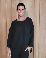 Remerón negro de corte holgado con textura sutil, cuello redondo, mangas tres cuartos y bolsillo frontal. Presenta un diseño asimétrico con el ruedo trasero más largo que el delantero.