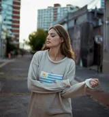 Sweater de hilo de algodón en color beige con diseño tejido de la bandera de Uruguay en el centro. Presenta cuello redondo, mangas largas y un corte holgado.