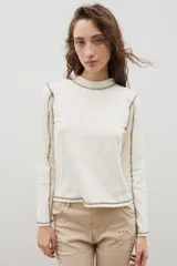 Remera de manga larga color crudo con cuello tipo tortuga y costuras a la vista en contraste de color marrón. Diseño de corte recto y estilo minimalista.