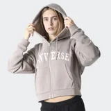 Campera tipo hoodie con cierre frontal, color gris topo, con capucha ajustable y logo de la marca estampado en el frente. Diseño de corte cropped y mangas largas.
