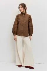 Camisa de manga larga color marrón, con cuello alto con volados, botonadura frontal y detalles calados en las mangas abullonadas.