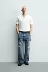 Pantalón de jean estilo carpintero con corte relaxed fit, tiro medio y pierna recta. Presenta un lavado azul medio con efecto desgastado y roturas en las rodillas. Incluye bolsillos laterales tipo plastrón, tira multifunción en la pierna, cierre frontal con cremallera y botón.