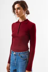 Top de tejido de punto acanalado color bordó, de manga larga y cuello polo con botones frontales.