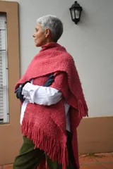 Ruana de lana merino tejida en telar, con diseño de rayas verticales en tonos crudo y rojizo, y terminación de flecos en el ruedo.