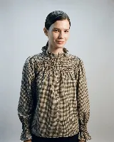 Camisa de lana a cuadros con diseño romántico. Presenta un canesú con bordado y frunces, cuello con volado y cierre frontal con botones de nácar. Las mangas son largas con puños elásticos fruncidos que terminan en un pequeño volado.