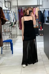Vestido largo negro confeccionado en crepé y gasa, de corte al cuerpo con escote recto, tiritas finas y falda larga semitransparente con tajo lateral pronunciado. Incluye accesorio tipo corbatín a juego.