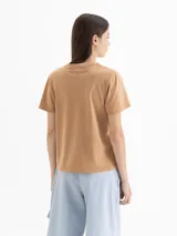 Remera de algodón color marrón con estampa frontal que incluye texto, flores, flechas y un patrón de rombos. Presenta cuello redondo y mangas cortas.