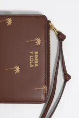 Billetera monedero de piel color marrón de Bimba y Lola, con estructura rígida y estampado de pequeñas palmeras doradas. Cuenta con cierre de cremallera superior con tirador de tela, logo impreso en el frente y tarjetero interior.