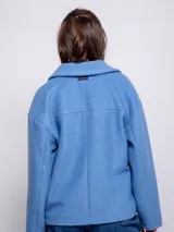 Tapado corto de paño con cuello camisero, cierre frontal de botones veteados y dos bolsillos frontales tipo parche. Presenta un diseño de corte recto y mangas largas.