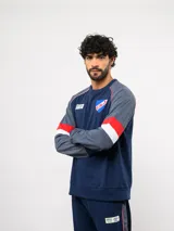 Buzo de cuello redondo del Club Nacional de Football, color azul marino con mangas grises y franjas rojas y blancas en los brazos. Incluye el escudo del club en el pecho y logos de Umbro y BBVA.
