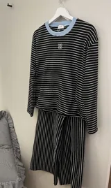 Pijama set de dos piezas compuesto por una remera de manga larga a rayas horizontales con cuello redondo celeste, y un pantalón largo de corte holgado a rayas verticales con cordón de ajuste en la cintura.