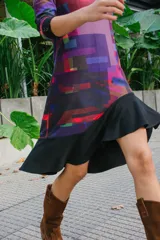 Vestido corto con estampado geométrico en tonos violeta, rojo y negro, confeccionado en jersey elastizado con efecto gamuzado. Presenta cuello redondo y mangas 3/4 con puños abotonados. La falda es de corte irregular con volados.