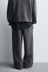 Pantalón jogger de corte wide fit confeccionado en tejido de algodón con interior de rizo. Presenta cintura elástica ajustable con cordón, bandas laterales decorativas, bolsillos laterales y un bolsillo trasero de plastrón. El acabado presenta un efecto lavado que le otorga una apariencia única.
