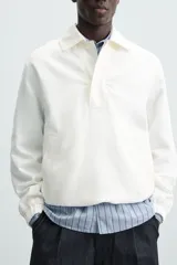 Cazadora tipo canguro de calce relajado, color blanco roto o crema, confeccionada en mezcla de lyocell y algodón. Presenta cuello solapa con cierre frontal de botonadura oculta, manga larga con puños elásticos y bolsillos frontales de vivo. El bajo es ajustable con elástico oculto en los laterales.