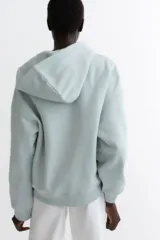 Campera con capucha de felpa color celeste, corte holgado con hombros caídos, cierre frontal y bolsillos delanteros tipo canguro.