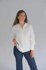 Blusa blanca de manga larga con cuello mao y cierre frontal de botones. Presenta detalles de bordados decorativos en los laterales del frente y puños anchos.