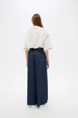 Pantalón de jean azul oscuro, tiro alto, corte ancho y holgado, con bolsillos y frunces en la cintura.