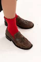 Mocasín de cuero color chocolate con acabado texturizado y diseño enrejillado en la capellada. Presenta horma cuadrada, taco bajo y suela de goma.