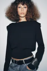 Jersey negro de punto, manga larga, con cuello redondo y detalle de pliegues o volados en la zona de los hombros.