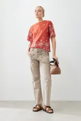 Remera de algodón color terracota con detalles de bordado broderie blanco en mangas y ruedo. Presenta cuello redondo y mangas cortas.