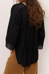 Camisa de lino color blanco, con escote en V, mangas tres cuartos con detalles de encaje en los puños y ruedo asimétrico más largo en la parte trasera.
