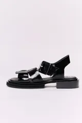 Sandalias negras de cuero charol con plataforma y taco bajo. Presentan tiras anchas con hebilla cuadrada grande en el empeine y tira de sujeción en el talón.