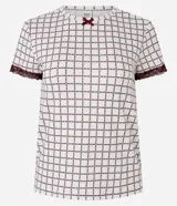 Blusa de pijama de cuello redondo y manga corta, confeccionada en tejido peach touch color blanco con estampado geométrico de corazones en tono bordó. Cuenta con detalles de encaje en los puños y un pequeño moño decorativo en el escote.