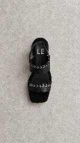 Sandalias de cuero marrón con punta cuadrada, tiras texturizadas con detalles de ojales metálicos y cordones entrelazados, y tira ajustable con velcro en el talón.