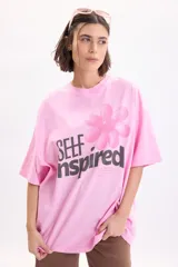 Remera oversize de manga corta en color rosado, con estampado gráfico frontal de una flor y la frase "Self Inspired" en tonos oscuros.