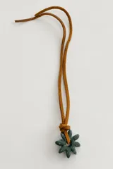 Collar de diseño artesanal con cordón de cuero tostado y dije de cerámica verde en forma de flor.