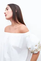 Blusa blanca con escote bardot y mangas cortas abullonadas con bordados dorados.
